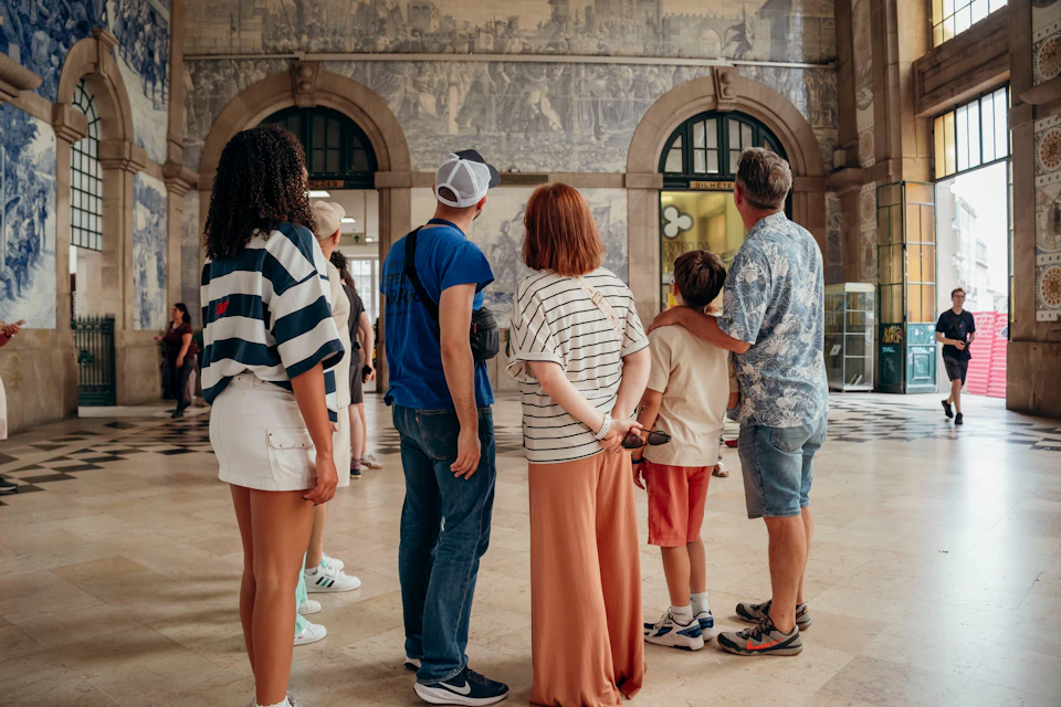 A group of people stands facing a mural inside a building with arched windows and a checkered floor.