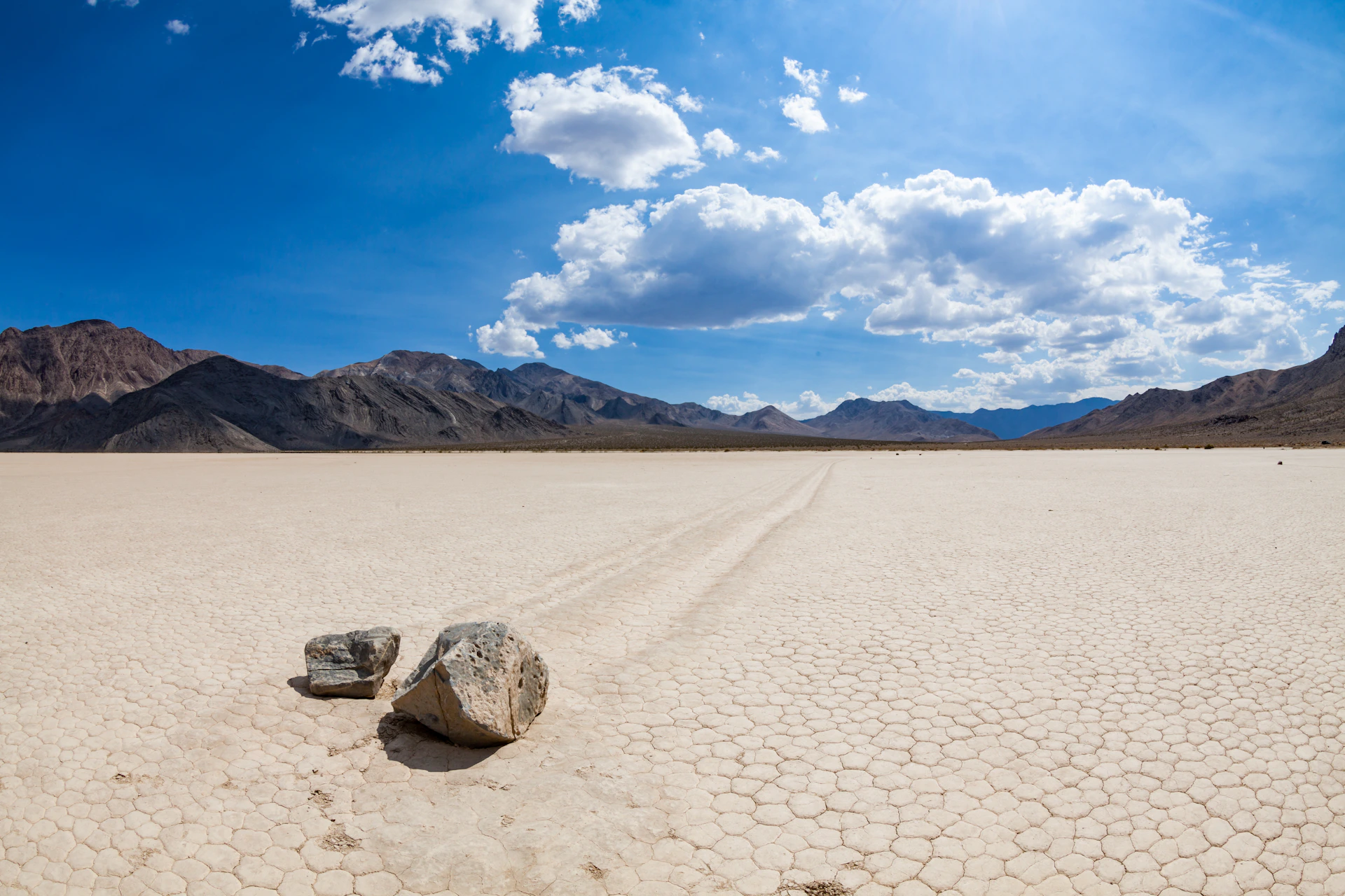 Two rocks on a dry, cracked ground with distant mountains under a partly cloudy sky.
