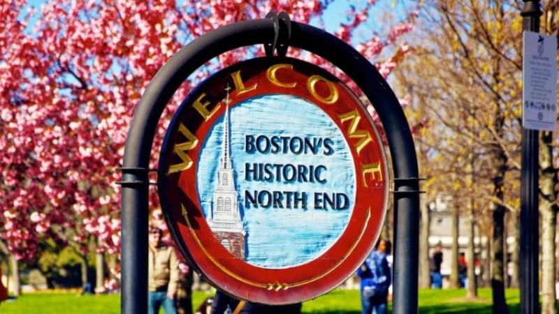 A round sign with the text "Welcome Boston's Historic North End" and an image of a church steeple, set against spring foliage.