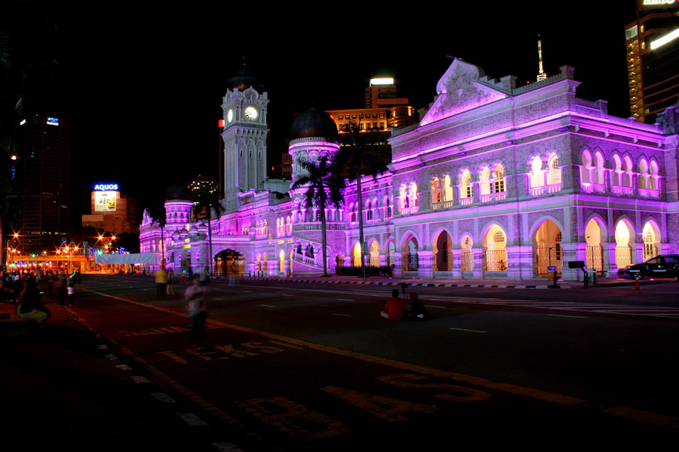 A historic building illuminated with colorful lights at night, featuring arched windows and a clock tower.