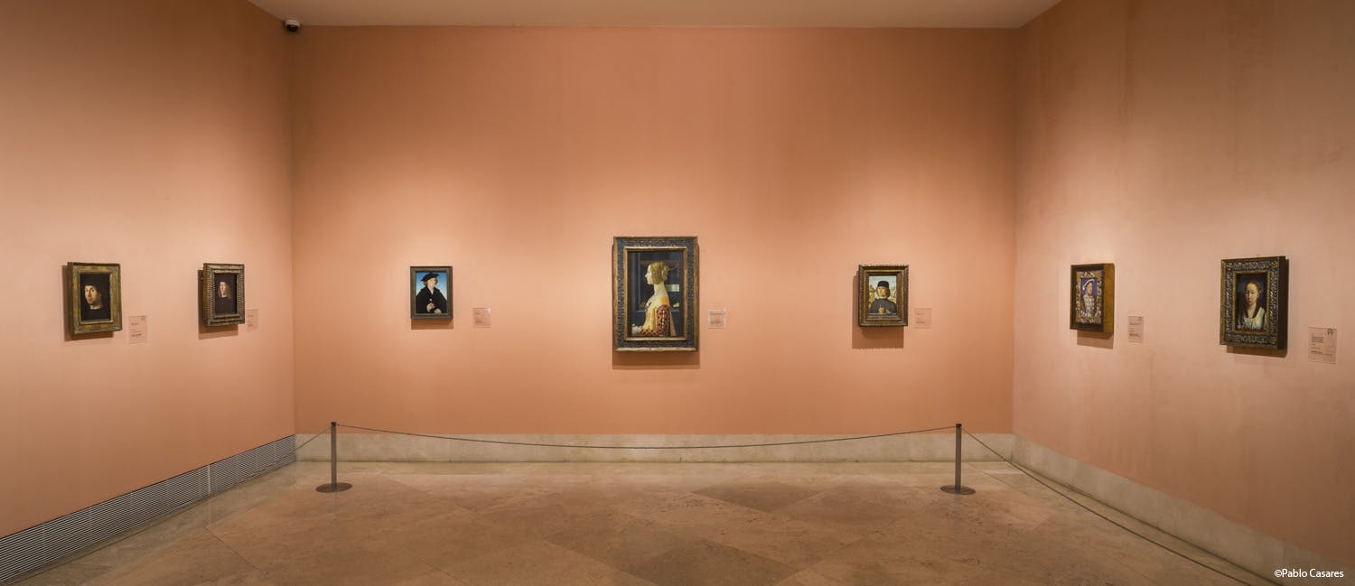 예술 갤러리의 복숭아 색 벽에 세 개의 액자 그림이 걸려 있으며, 그 옆에는 정보용 명판이 있습니다.