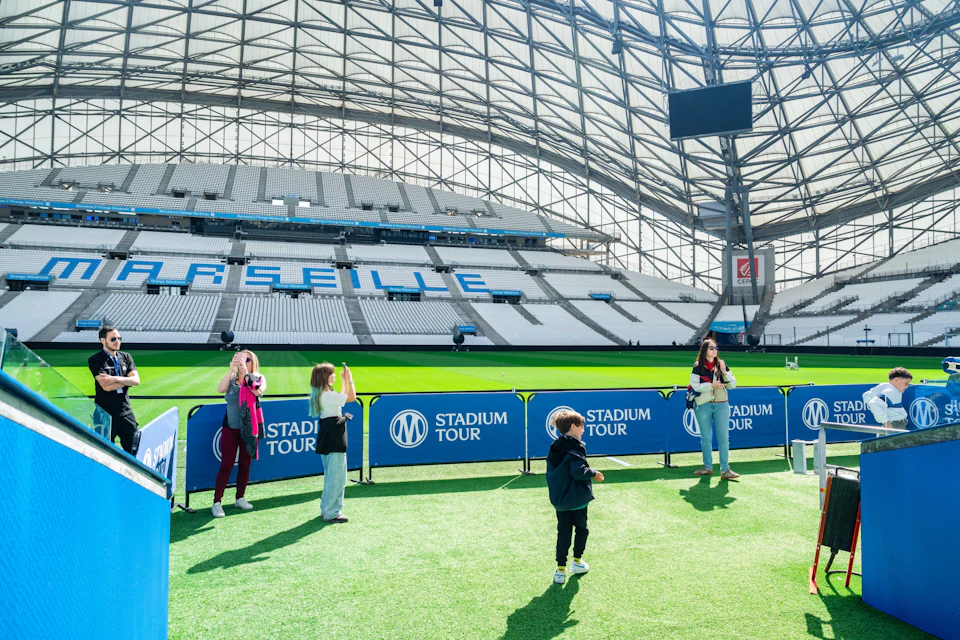 People stand on the field of a modern stadium with a clear roof, taking photos and exploring during a stadium tour.