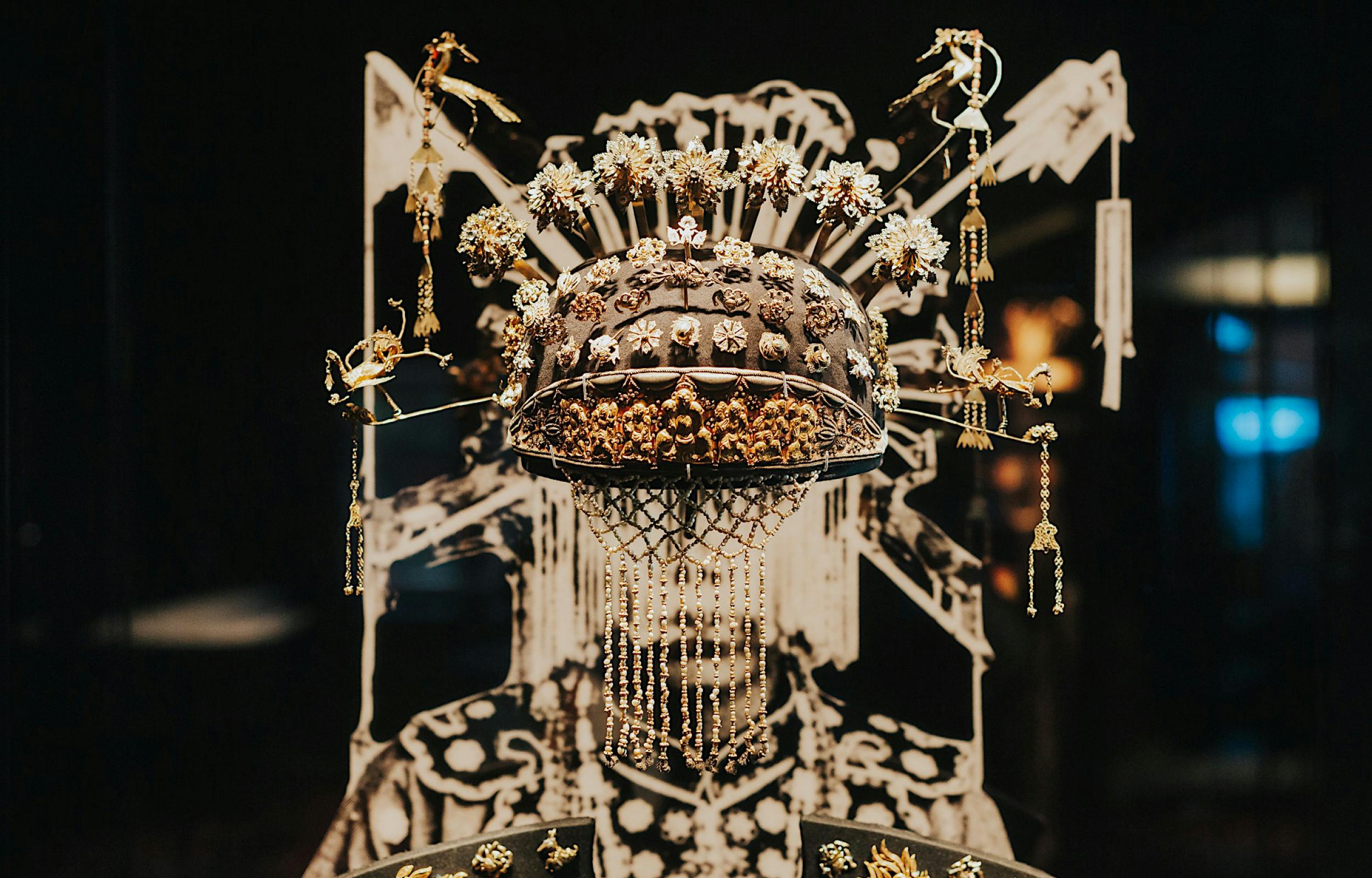 An ornate headdress adorned with intricate decorations, displayed against a detailed, patterned background.