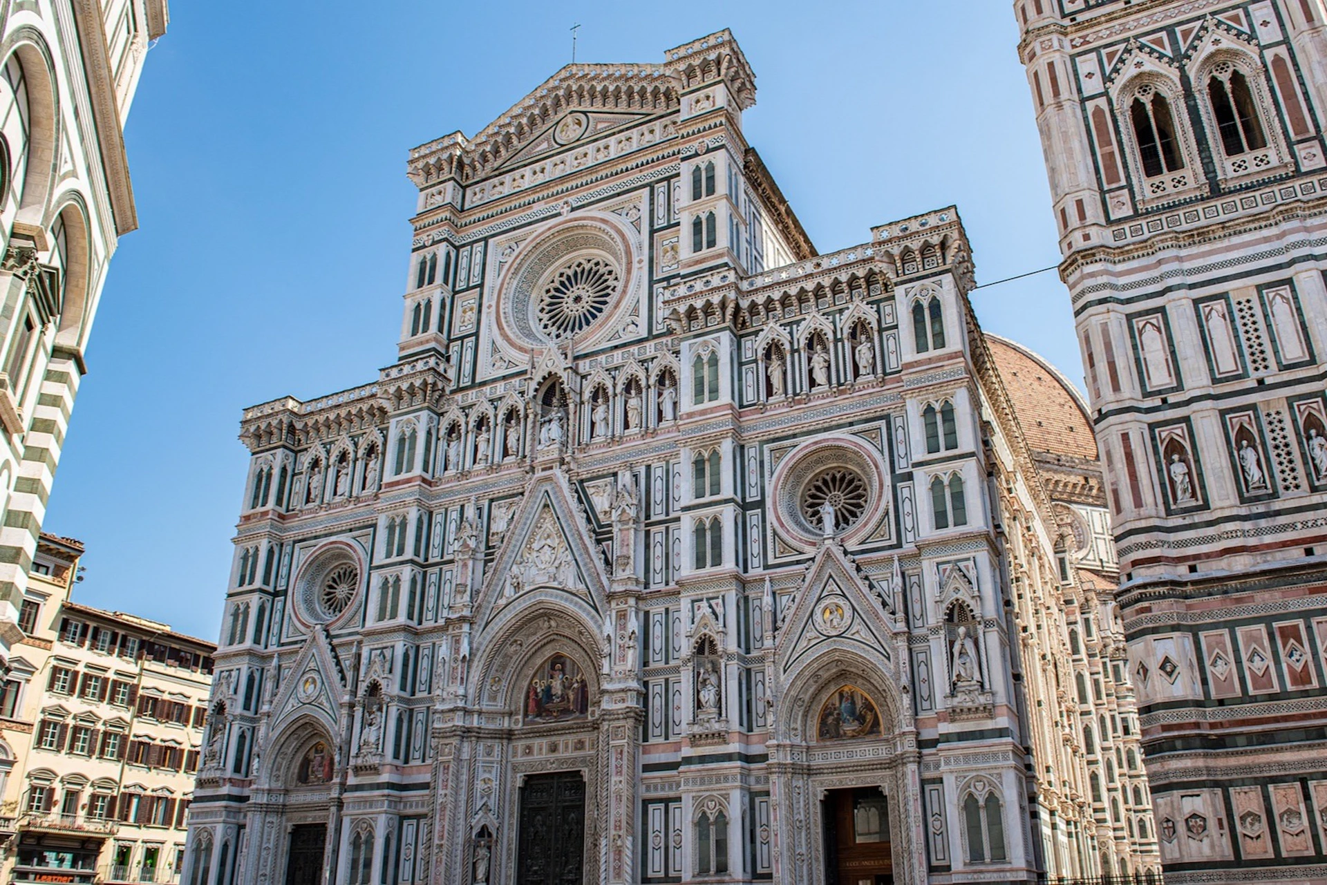 Elaborate cathedral facade with intricate designs, rose windows, and statues, set against a clear blue sky.
