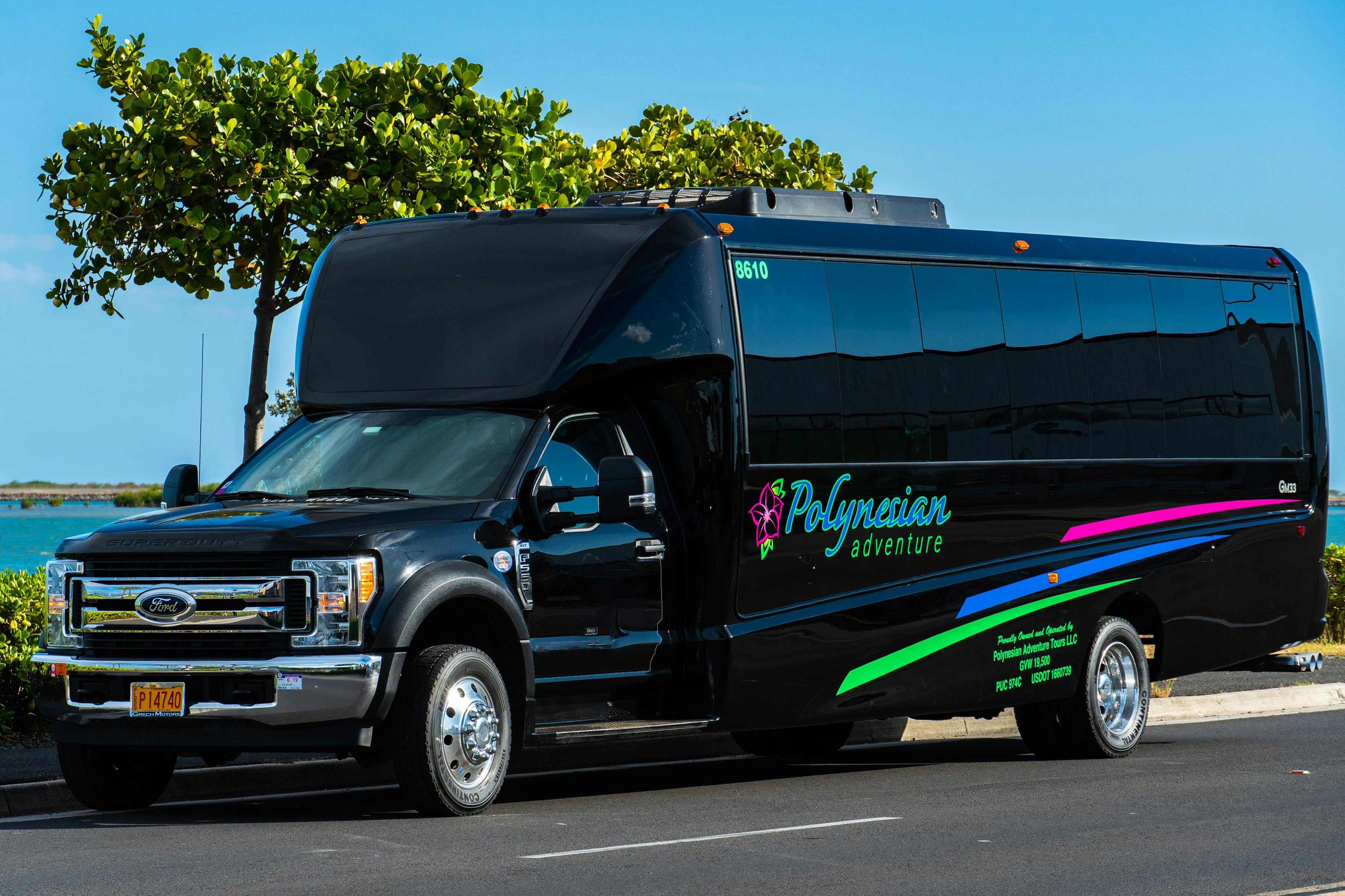 A black tour bus labeled "Polynesian Adventure" parked on a sunny street, with trees visible in the background.