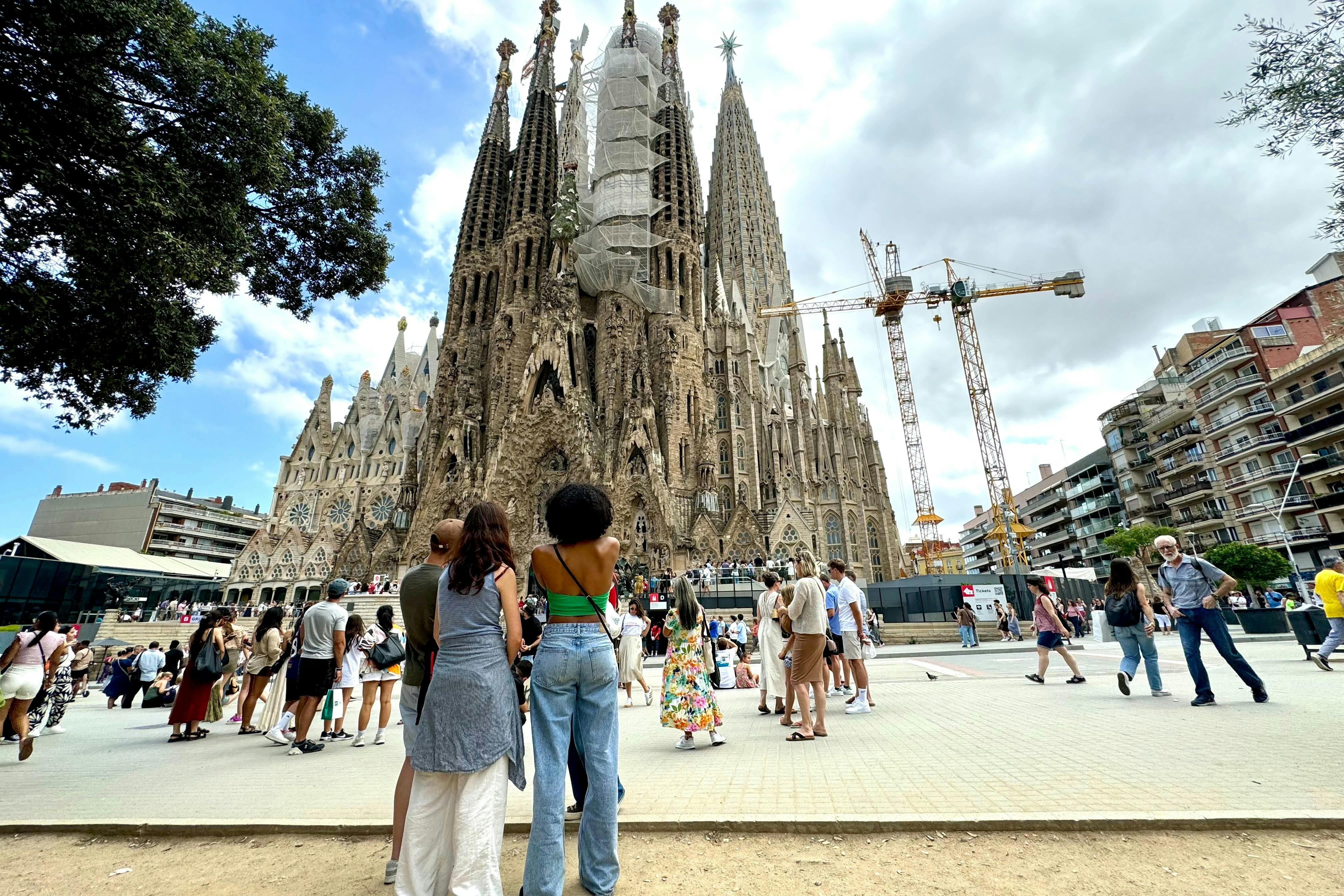 방문객들은 가우디의 미완성 대성당인 사그라다 파밀리아 (Sagrada Familia) 의 첨탑 앞에 서 있습니다.