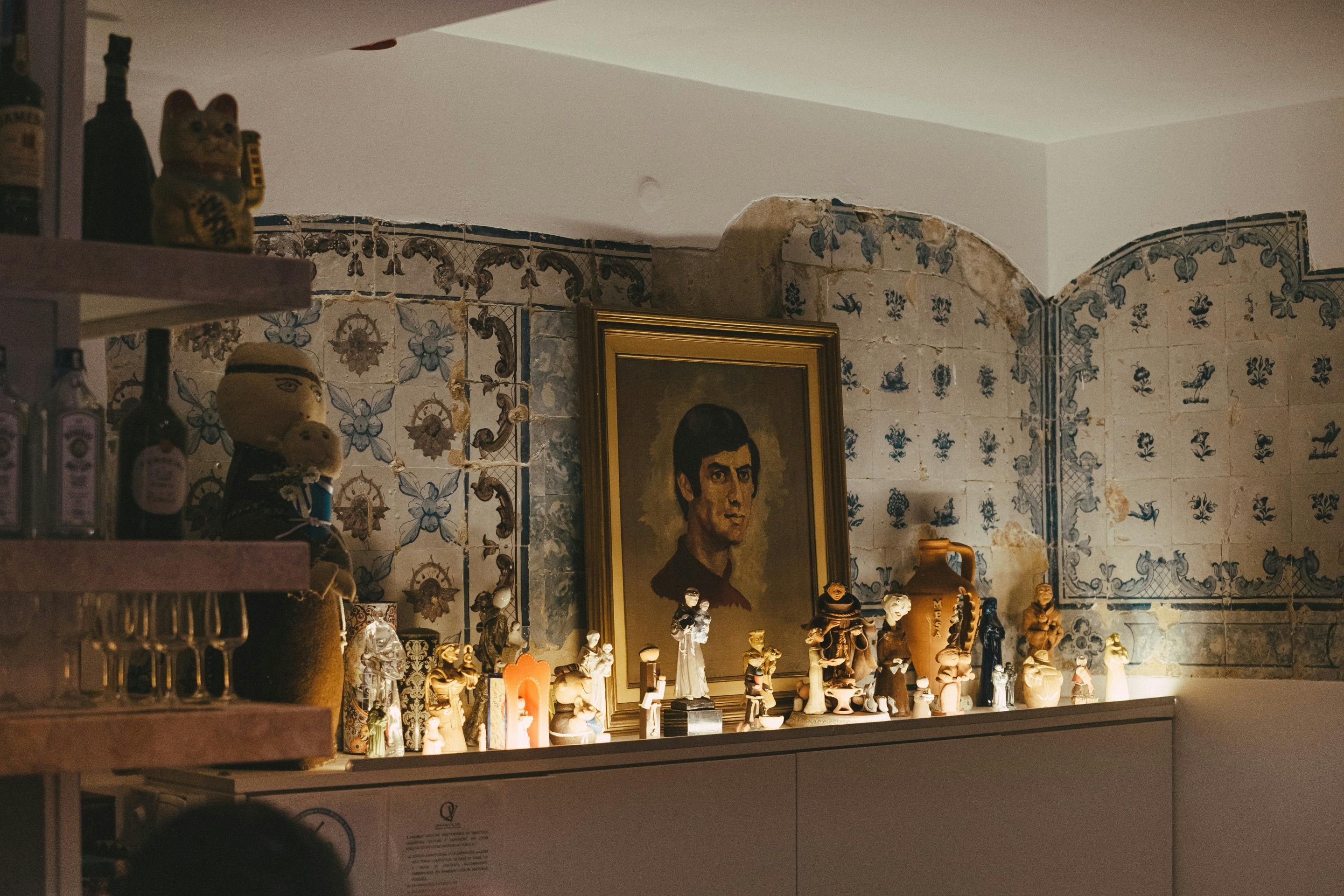 Ένα ράφι με πολλαπλά ειδώλια και ένα κορνιζαρισμένο πορτρέτο σε έναν γερασμένο τοίχο με σχέδια.