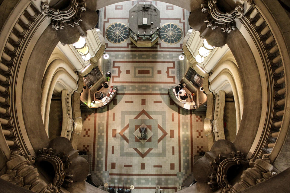 Ornate architectural interior from a high angle, showing a patterned floor, two desks, and people working with books.