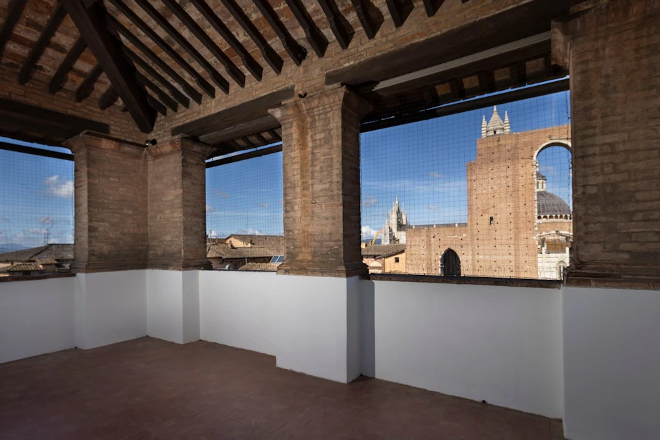 A terrace with brick columns and a view of a historical cityscape with a blue sky and cathedral spires in the distance.