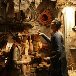 Två detaljerade figurer i tidstypiska kläder interagerar i en rustik miljö med hängande kött, korgar och en luta.