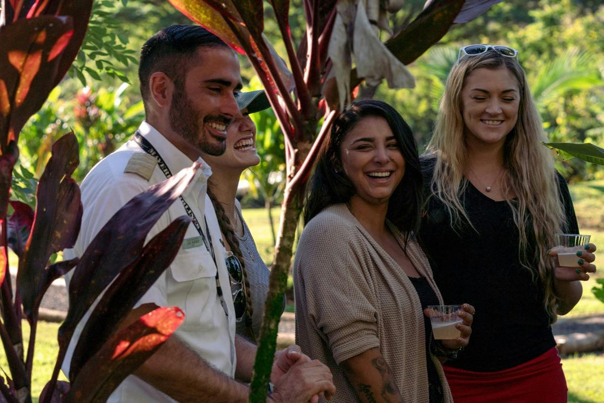 Four people smiling and standing outdoors surrounded by tropical plants, one holding a drink.