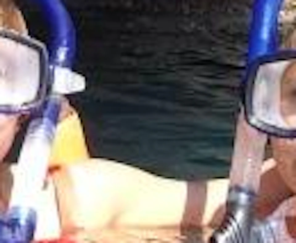 Two people wearing snorkeling gear float on the water's surface near the entrance of a cave.