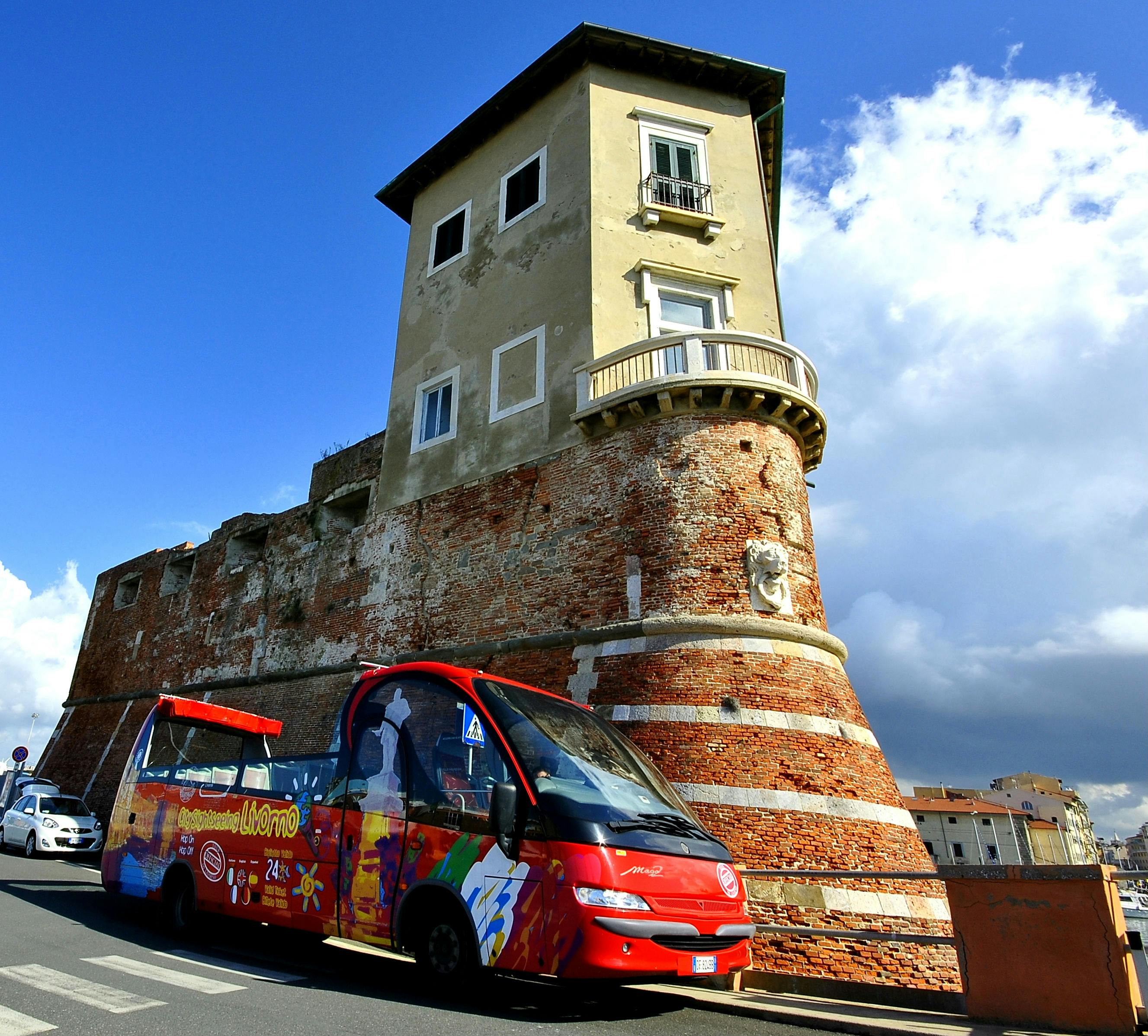Red tourist bus parked beside an old brick fortress tower under a blue sky with clouds.