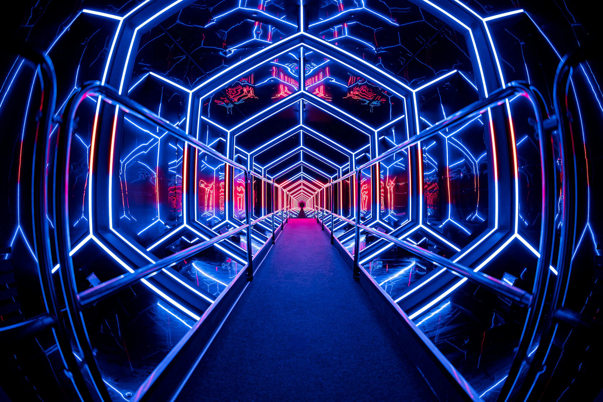 A tunnel with mirrored walls and a glowing geometric design in blue and red neon lights, creating a futuristic effect.