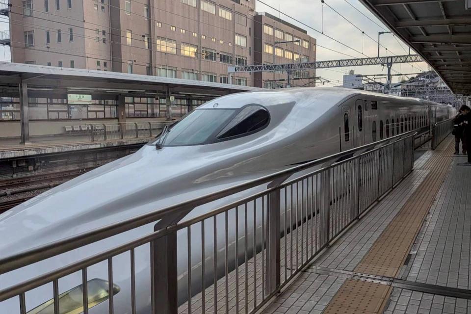 A sleek silver bullet train stopped at a station platform with a modern building in the background.