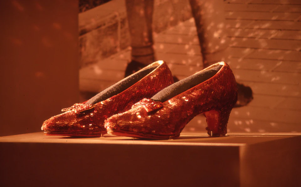 Sequined red high-heeled shoes with bows displayed against a blurred background featuring a black and white image.