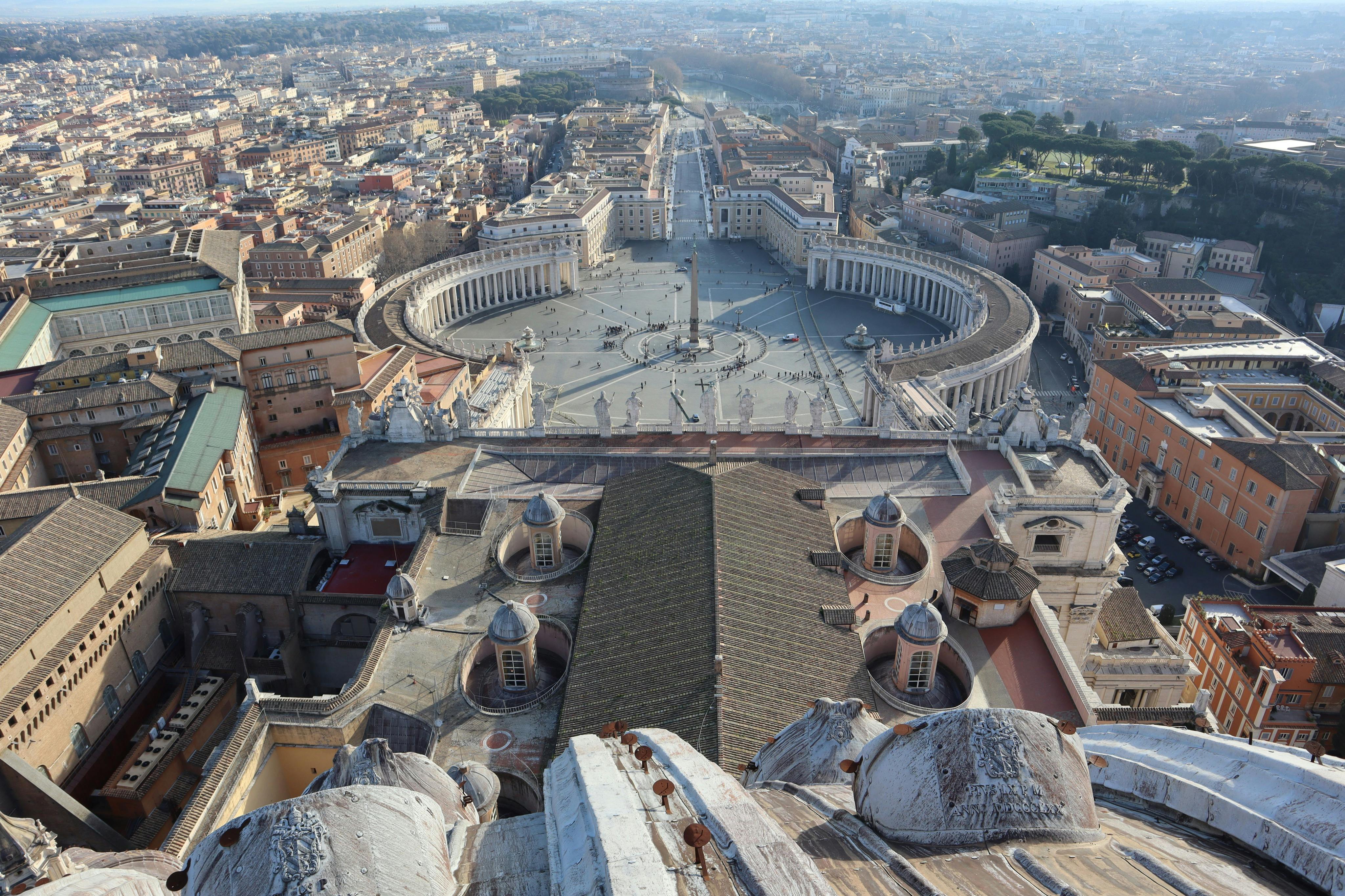 Una vista dall&#39;alto di Piazza San Pietro nella Città del Vaticano, che mostra i colonnati, l&#39;obelisco e il paesaggio urbano circostante.