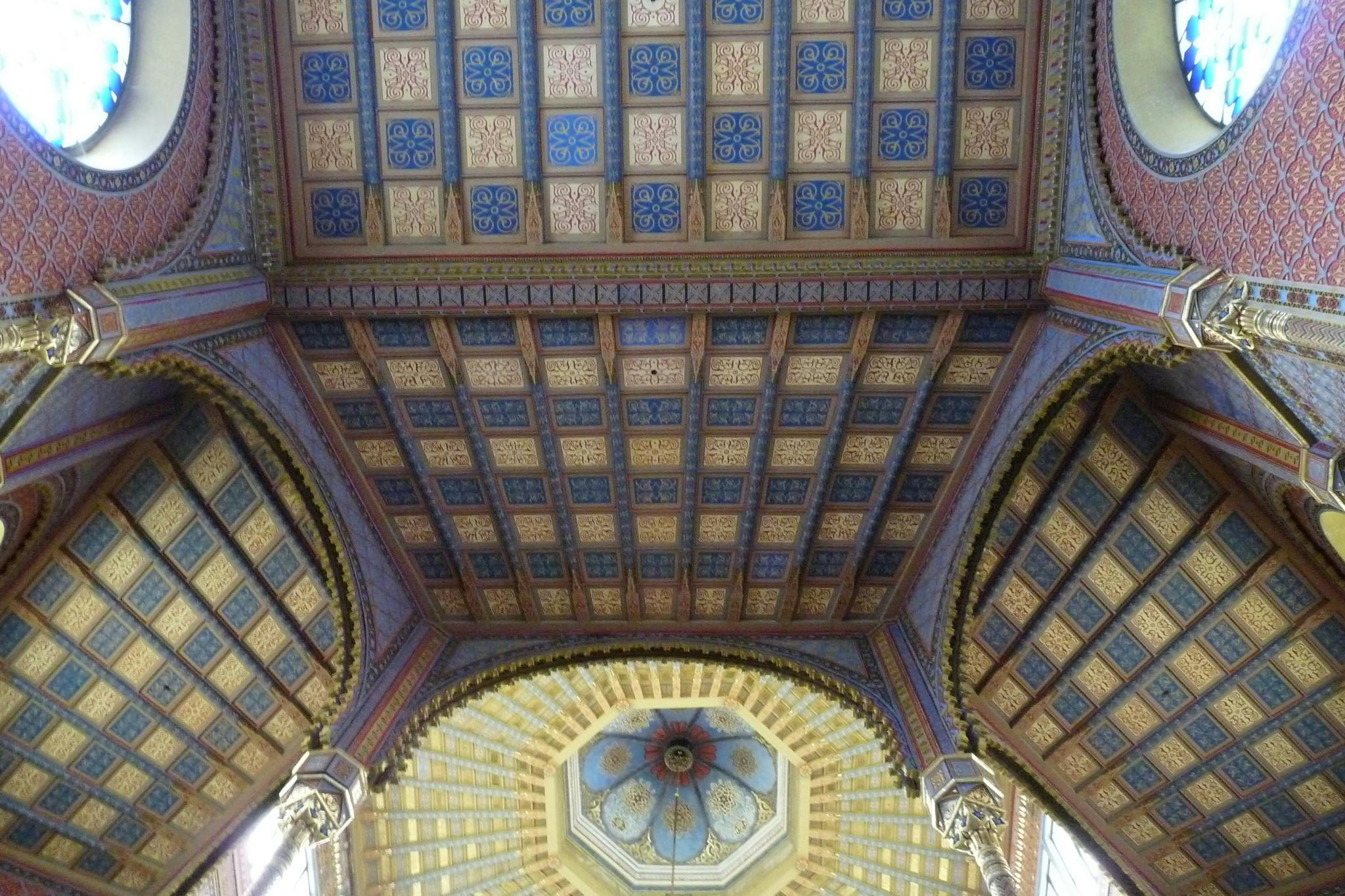 Intrikat utformat tak med färgglada geometriska mönster och en kupol prydd med konstnärliga detaljer i en historisk byggnad.