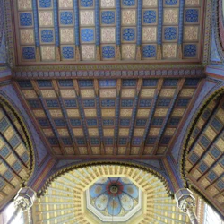 Intrikat utformat tak med färgglada geometriska mönster och en kupol prydd med konstnärliga detaljer i en historisk byggnad.