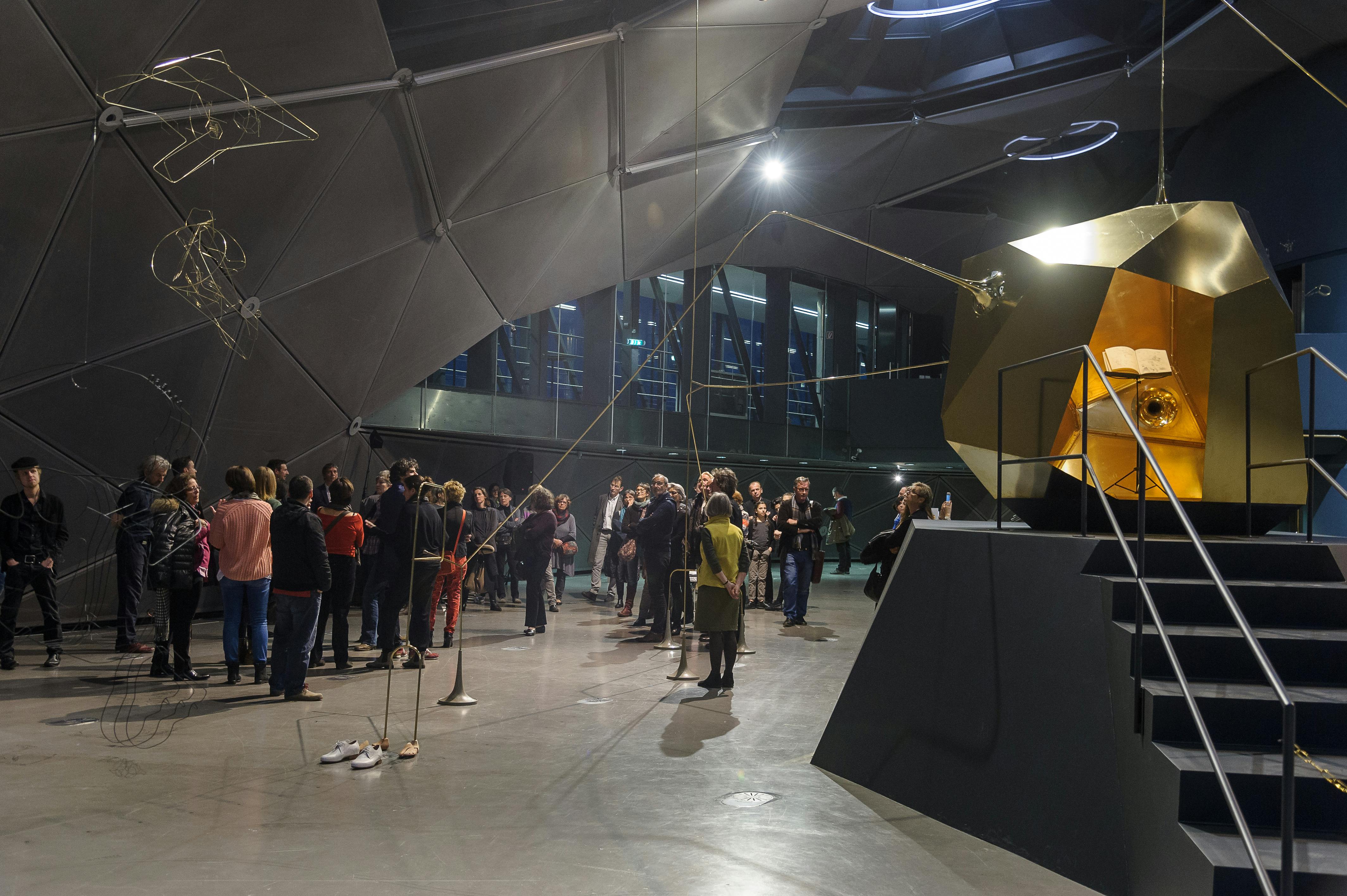 一群人聚集在一座现代化的几何建筑内，展出独特的雕塑和装置。