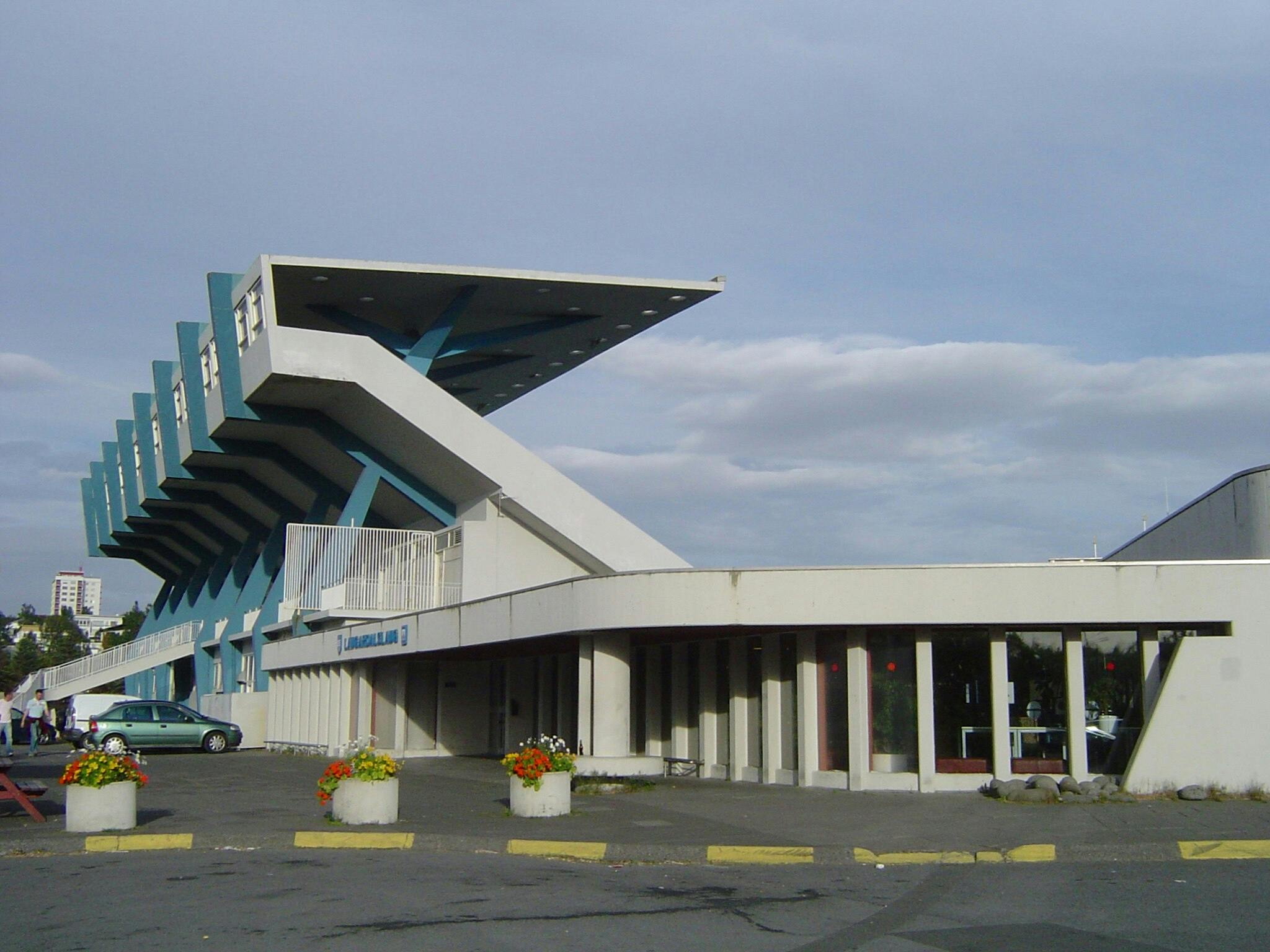 독특한 각진 지붕 디자인의 현대적인 흰색과 파란색 건물로, 커다란 창문과 앞에 꽃이 있는 화분이 있습니다.