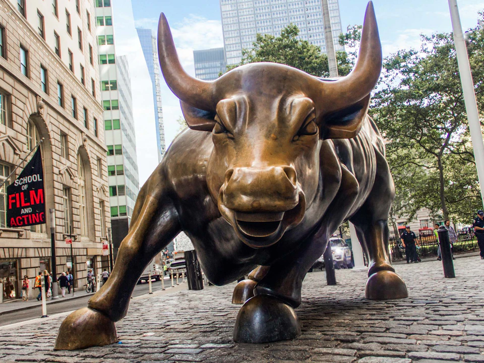 A bronze bull statue with outstretched legs and large horns on a cobblestone street between tall buildings.