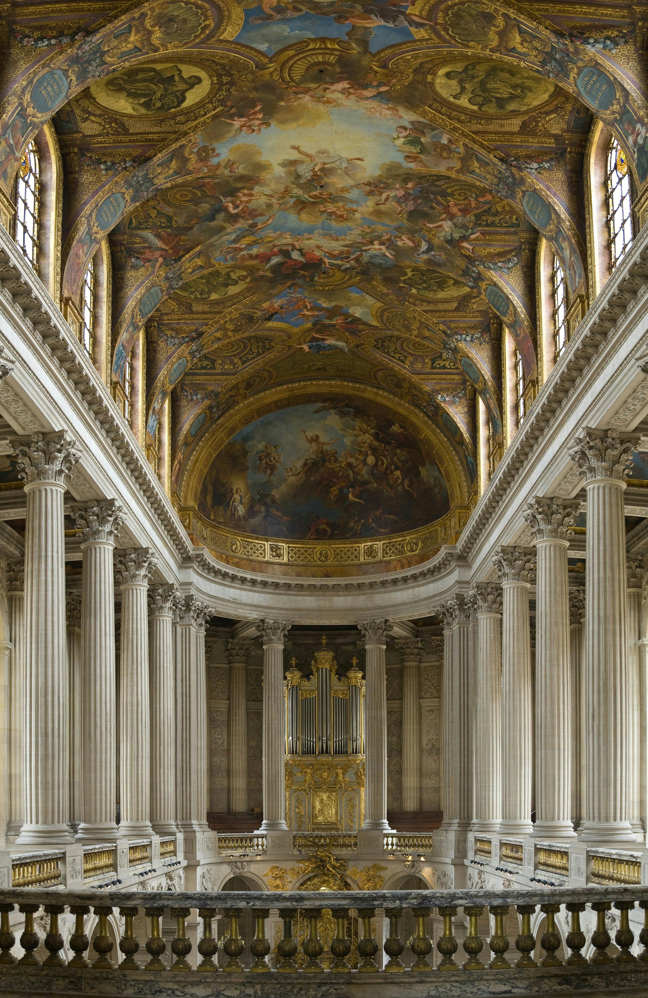 Ornate hall with tall columns, a grand ceiling adorned with elaborate frescoes, and a large gold-framed organ at the far end.