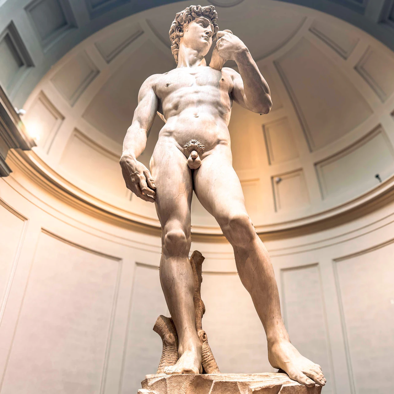 A marble statue of a standing male figure in a museum under a domed ceiling.