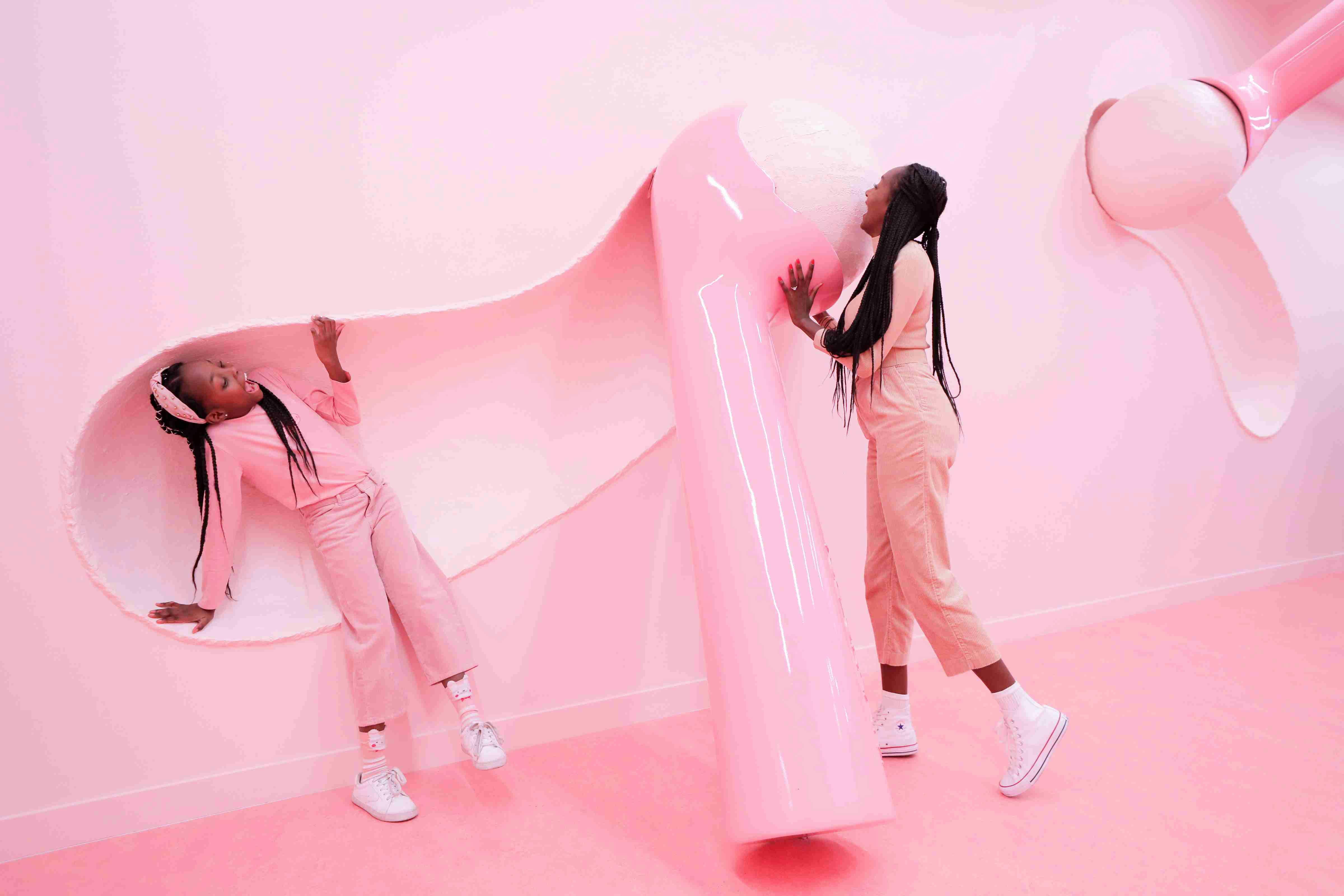 Two people dressed in pink interact with a giant pink sticky note installation on a monochromatic pink background.