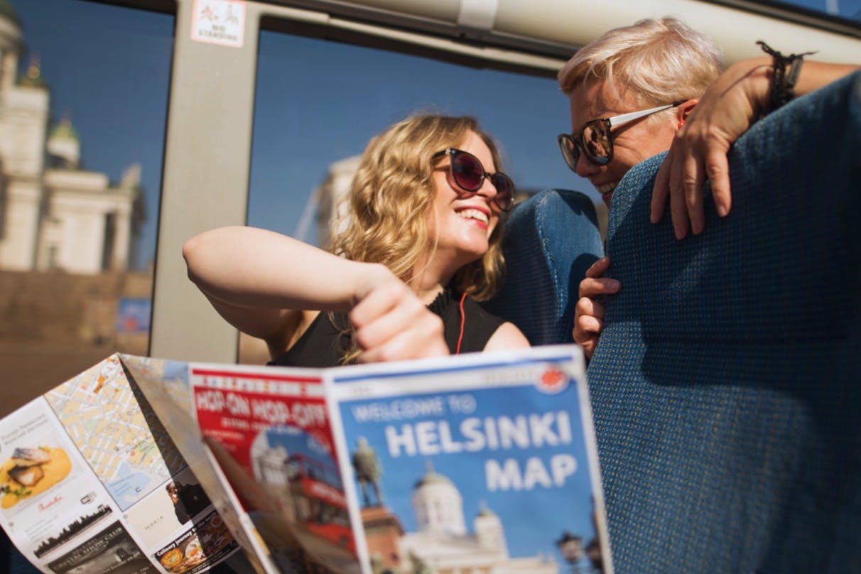 Dva lidé se usmívají a chatují v autobuse s helsinskou mapou v popředí.