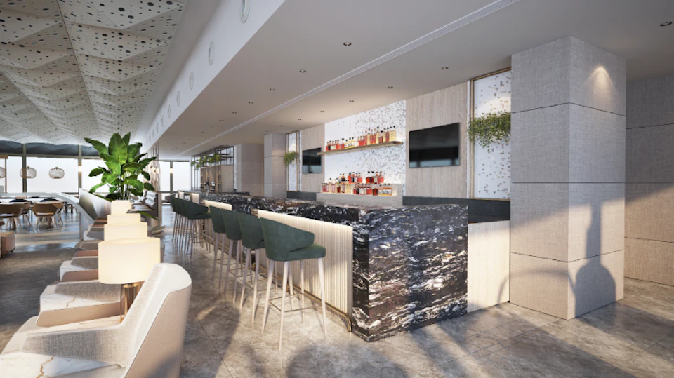 Modern bar with marble counter, green bar stools, shelves of liquor bottles, and two large screens on the wall, under soft lighting.