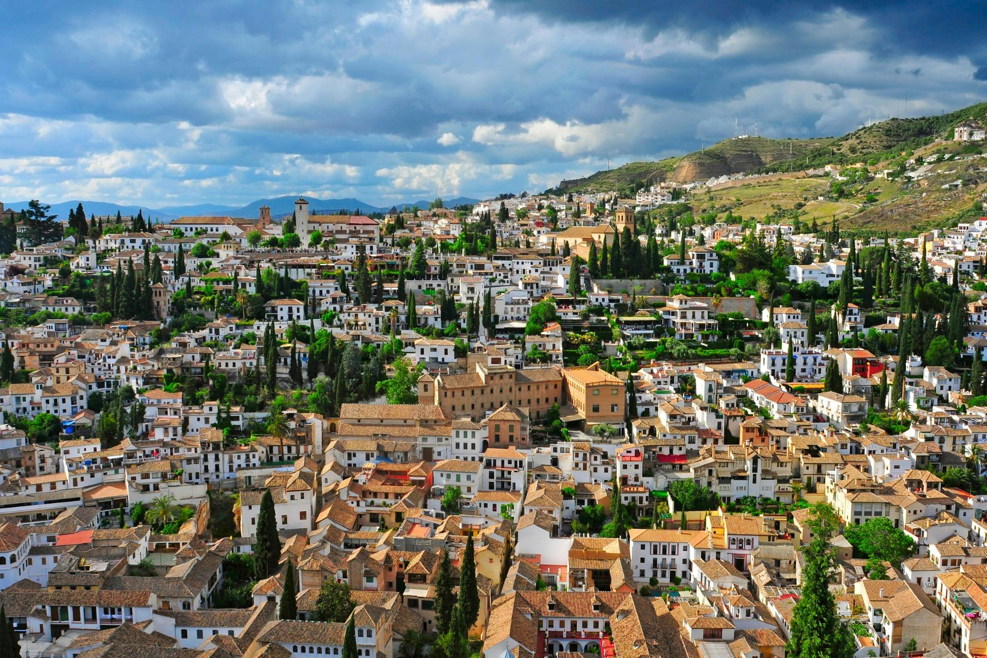 老城区的鸟瞰图，茂密的白色建筑，棕色的瓷砖屋顶，多云的天空下的绿色树木。