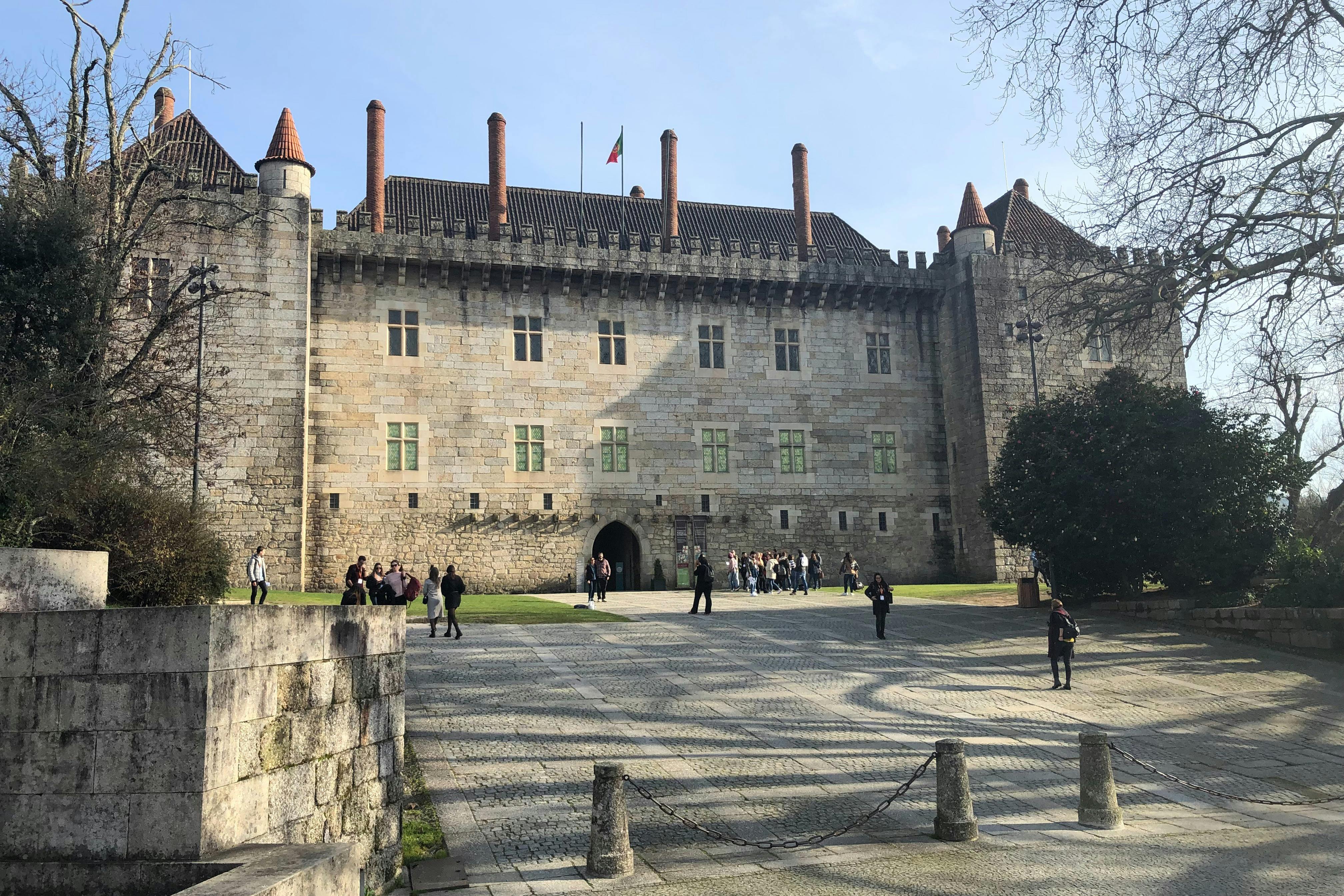 A historic stone castle with several turrets and a central courtyard where people are walking and gathering.