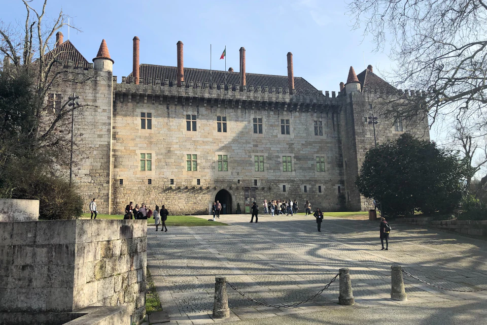 A historic stone castle with several turrets and a central courtyard where people are walking and gathering.
