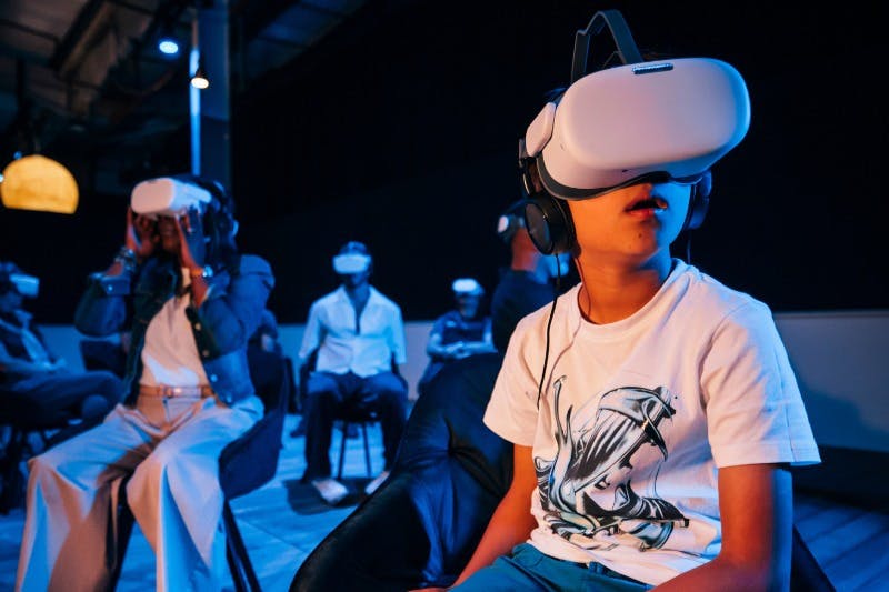 一群人，包括前景中的一个孩子，戴着虚拟现实耳机，坐在昏暗的房间里。