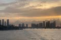 高層ビル、雲、黄色い太陽、静かな海に浮かぶ遠くのボートなど、マイアミのスカイラインは夕日に包まれています。