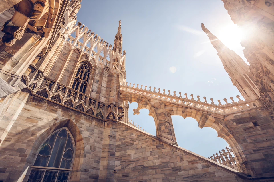 Close-up of detailed Gothic architecture with pointed arches and decorative elements, bathed in bright sunlight against a clear sky.