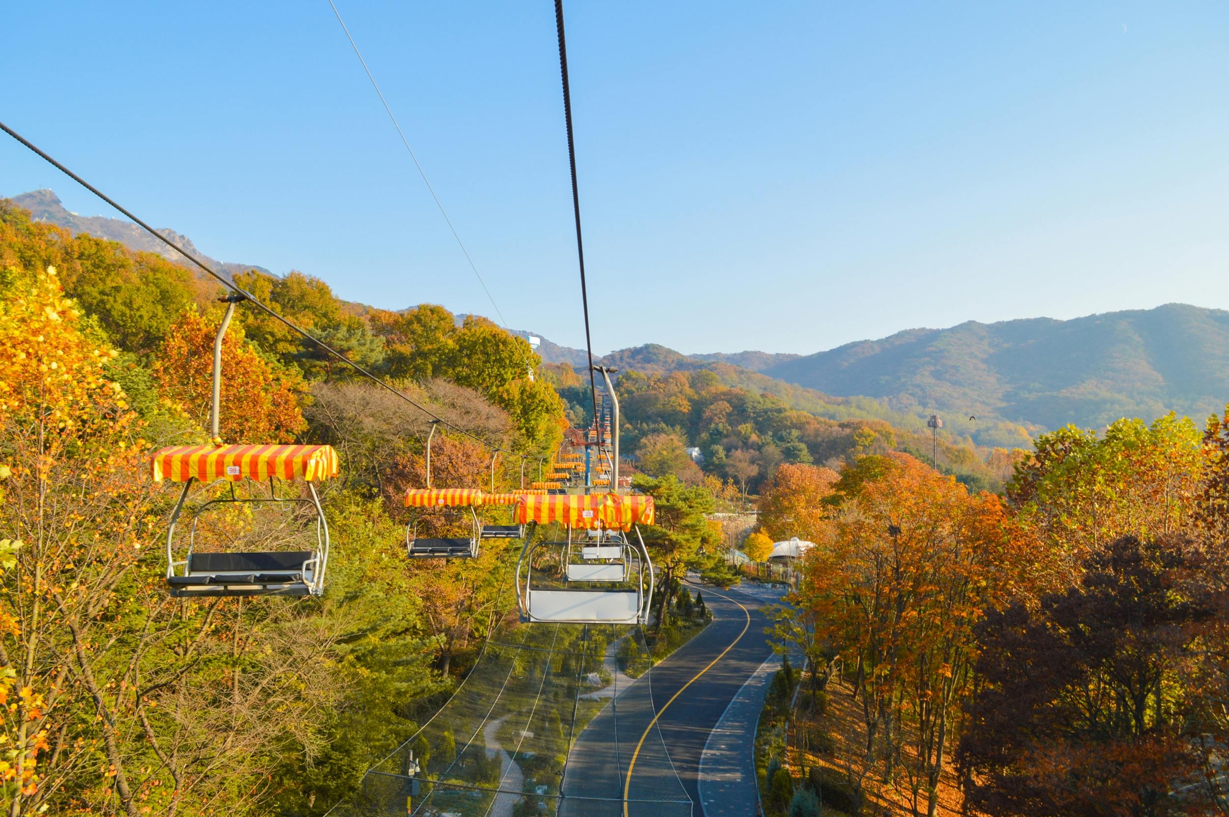 A chairlift with empty seats over a scenic autumn landscape with colorful trees and a winding road below.
