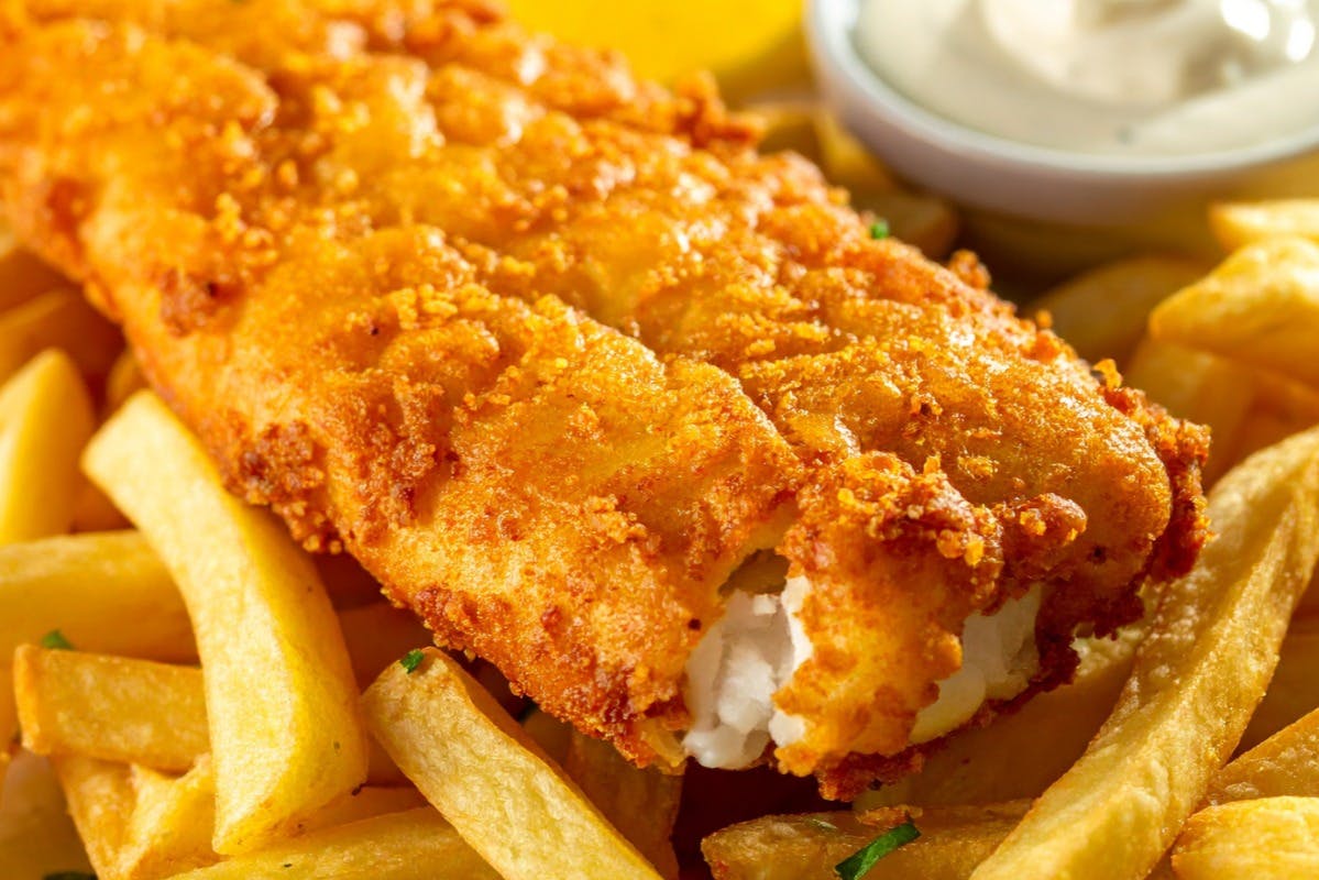 Τραγανό χρυσό τηγανητό ψάρι με μια μπουκιά έξω, σερβίρεται πάνω σε ένα κρεβάτι με πατάτες, με μια πλευρά σάλτσας ταρτάρ.