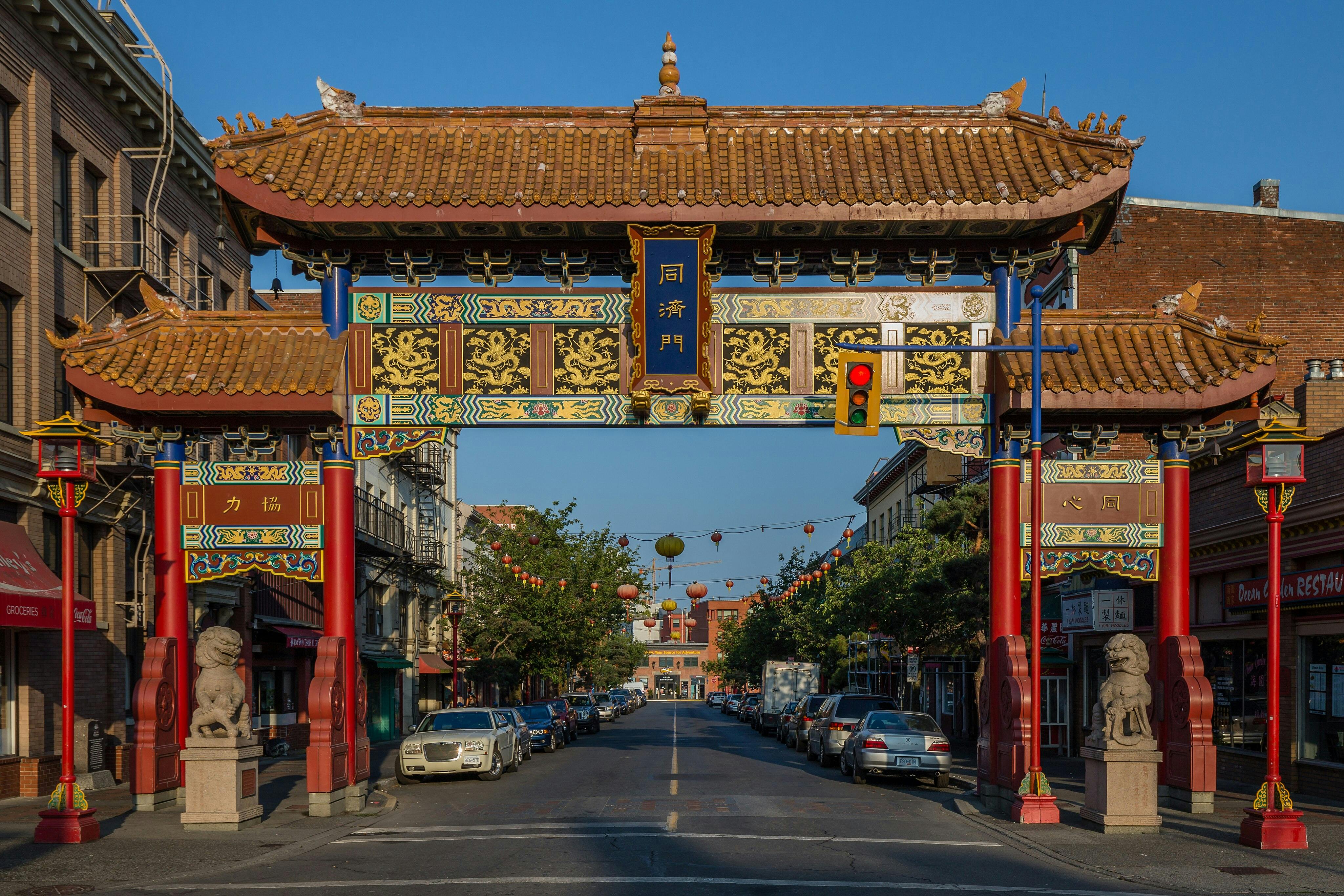 Porte chinoise ornée de statues de lions, de décorations vibrantes et de caractères chinois dans une rue animée bordée de voitures et de lanternes.