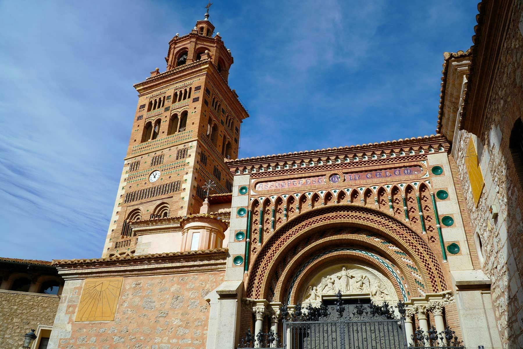 澄んだ青空の下には、複雑なデザインの細かいレンガの塔とアーチがあり、装飾的な時計が置かれています。