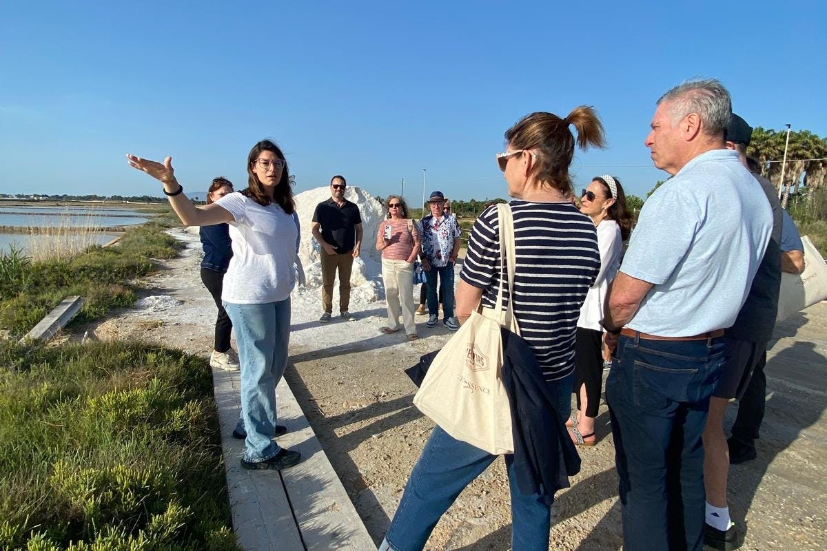 A group of people standing outdoors near a salt mound and greenery, with one person gesturing, under a clear blue sky.