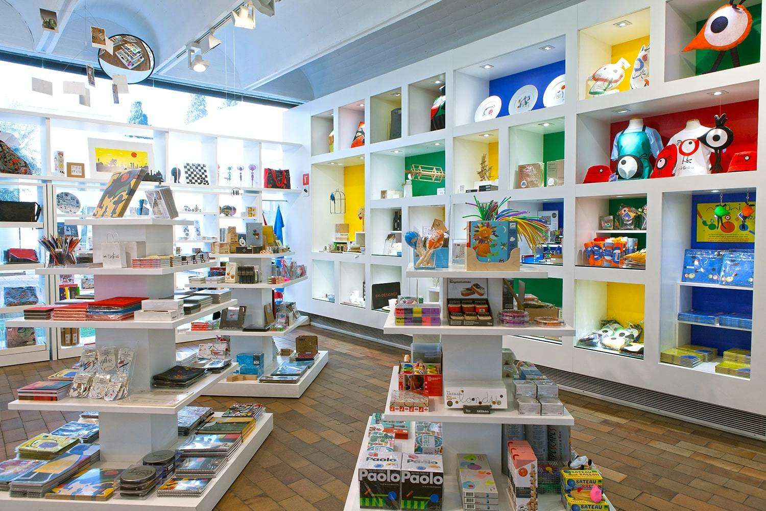 A well-lit gift shop with colorful shelves displaying a variety of toys, books, and gifts. White shelving units are organized neatly.
