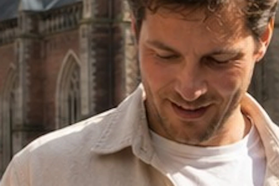 Three people smiling and looking at a smartphone in front of a large, historic church on a sunny day.