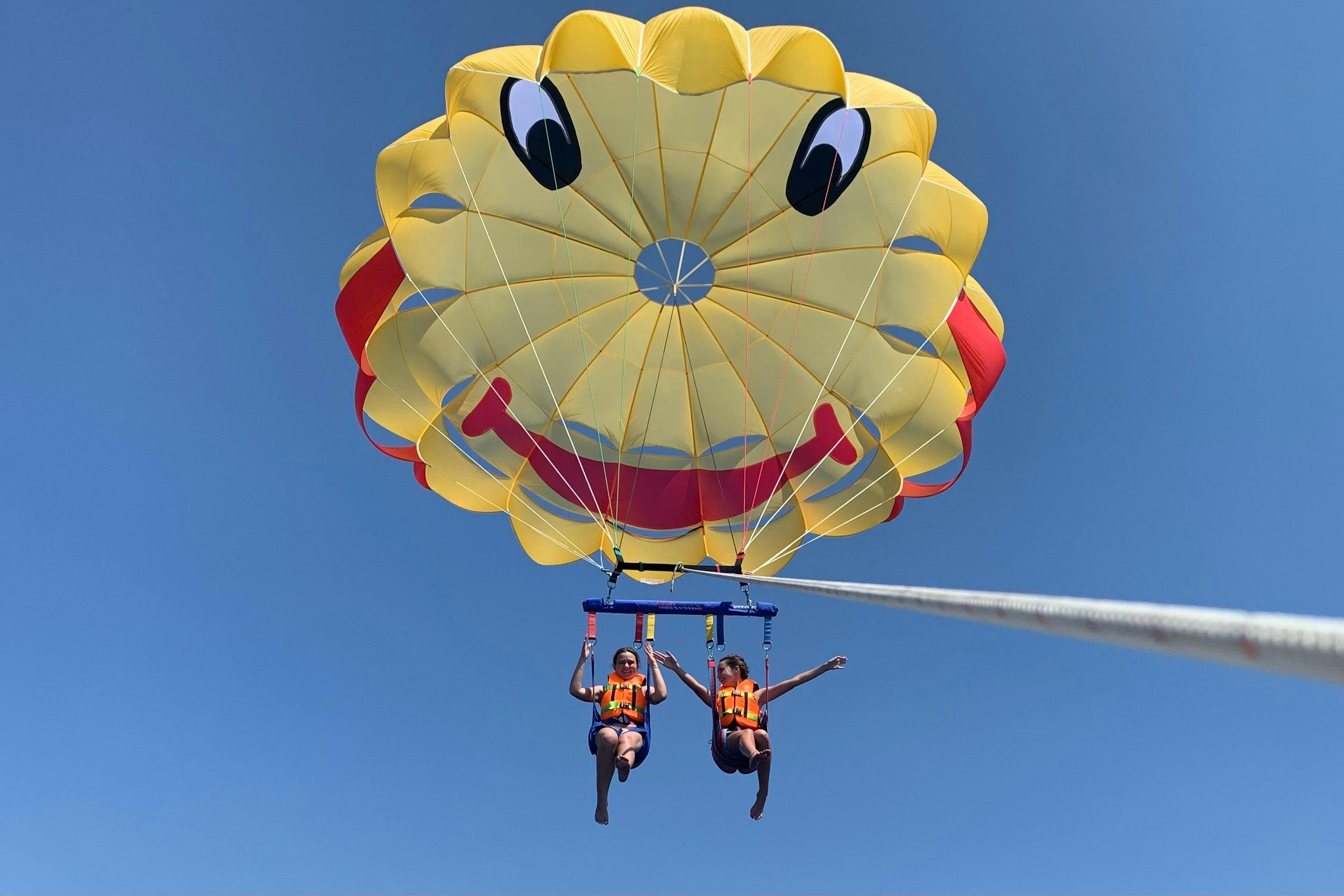 A smiley-face parasail during a parasailing flight with two people
