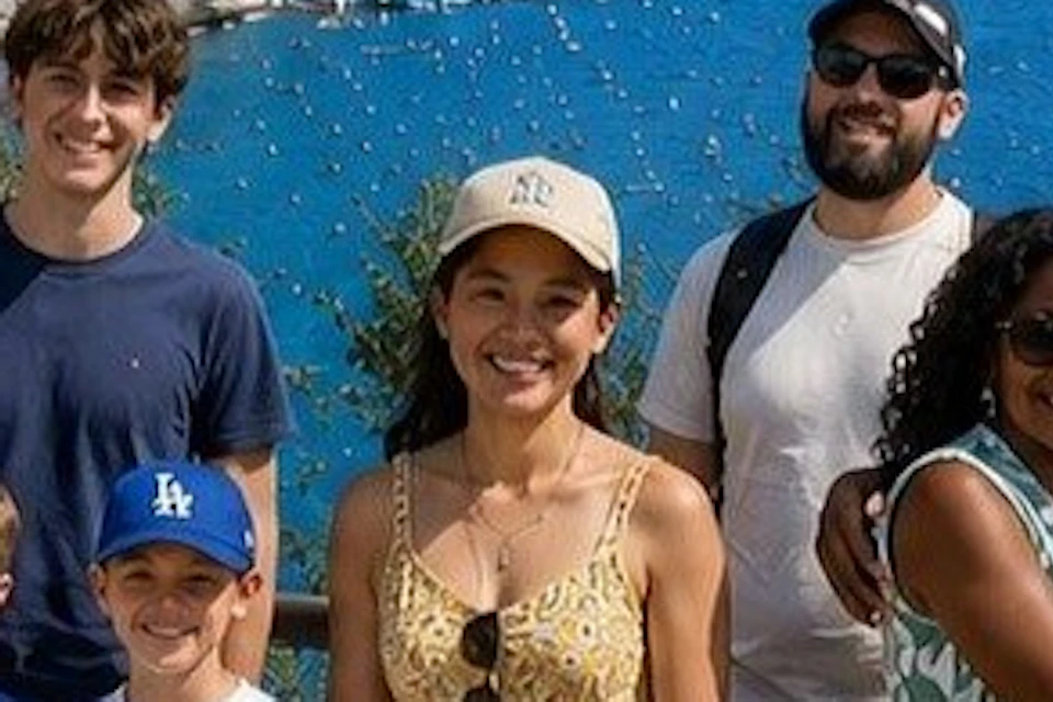 A group of people smiling and posing together by a coastal view with cliffs, buildings, and a blue sea in the background.
