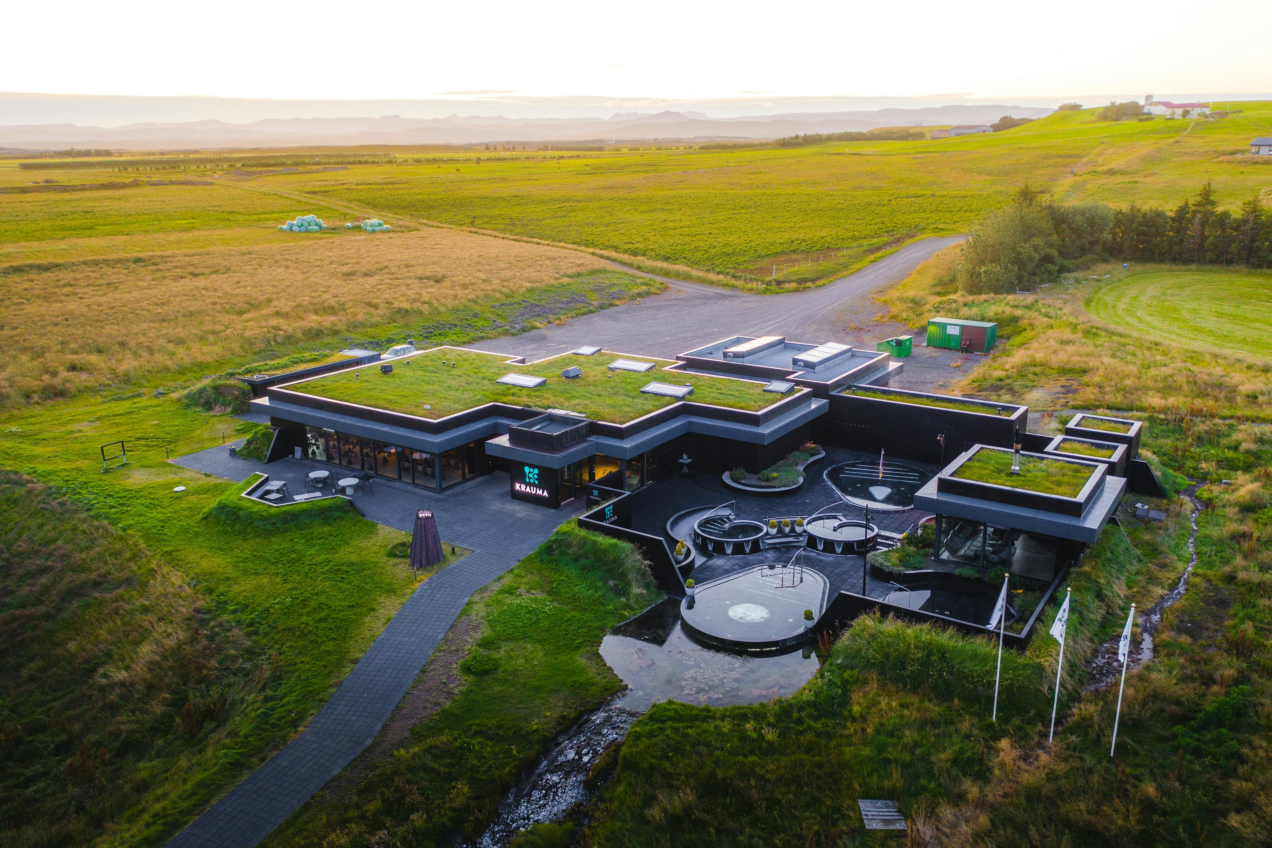 Ένα μοντέρνο κτίριο με στέγη από γρασίδι σε ένα καταπράσινο τοπίο με μονοπάτια και κυκλικό χώρο καθιστικού μπροστά.