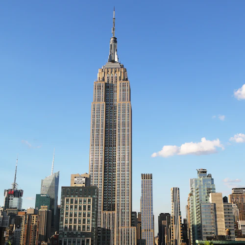 Hoher Wolkenkratzer mit einer Spitze, umgeben von anderen Hochhäusern unter einem klaren blauen Himmel mit ein paar Wolken.