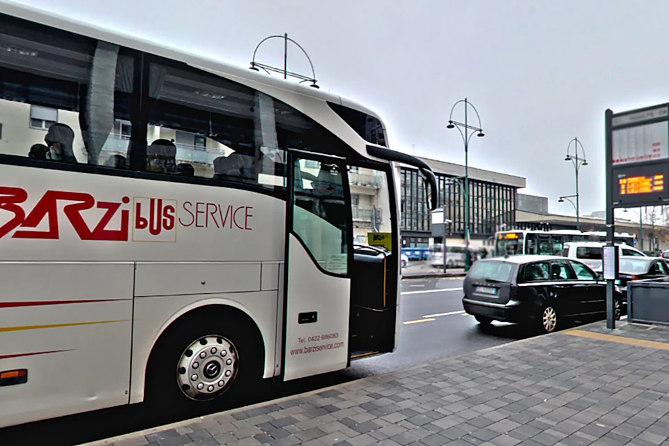 A bus labeled "Service" is parked on a city street with cars and buildings in the background.