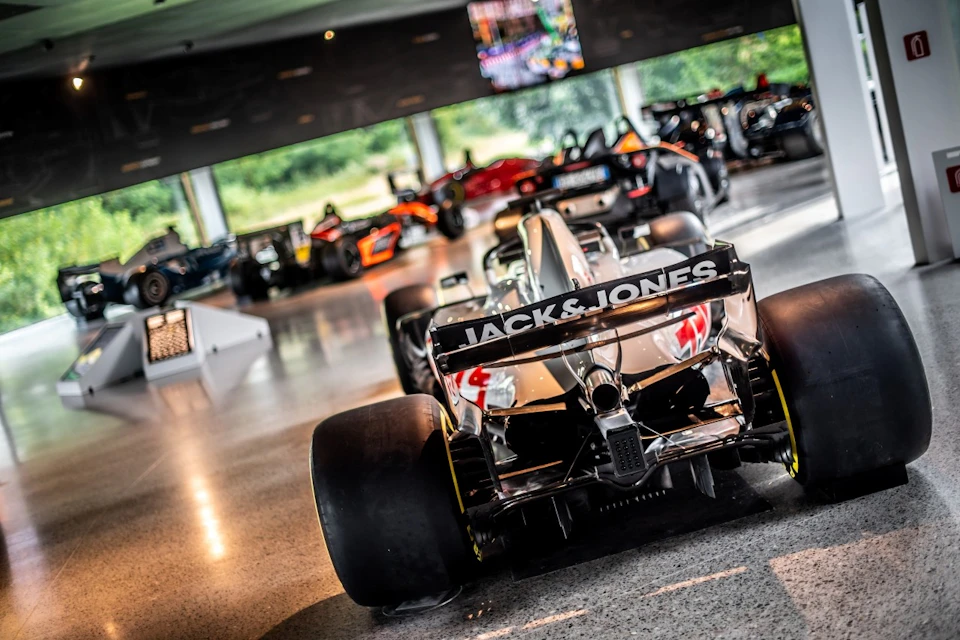 A collection of Formula 1 cars displayed indoors with a prominent car in the foreground labeled "Jack & Jones."